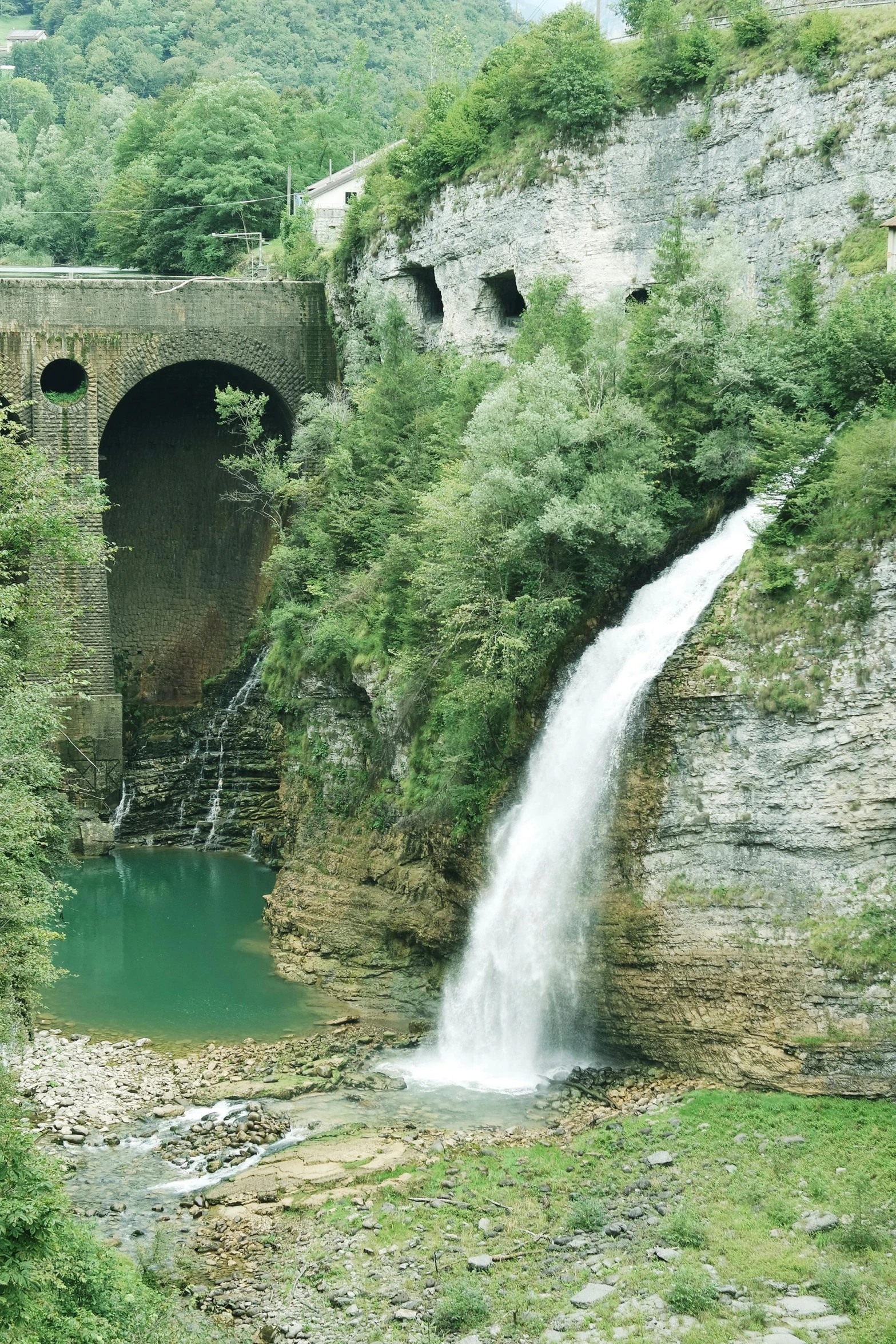 waterfall and bridge in a lush green area near water