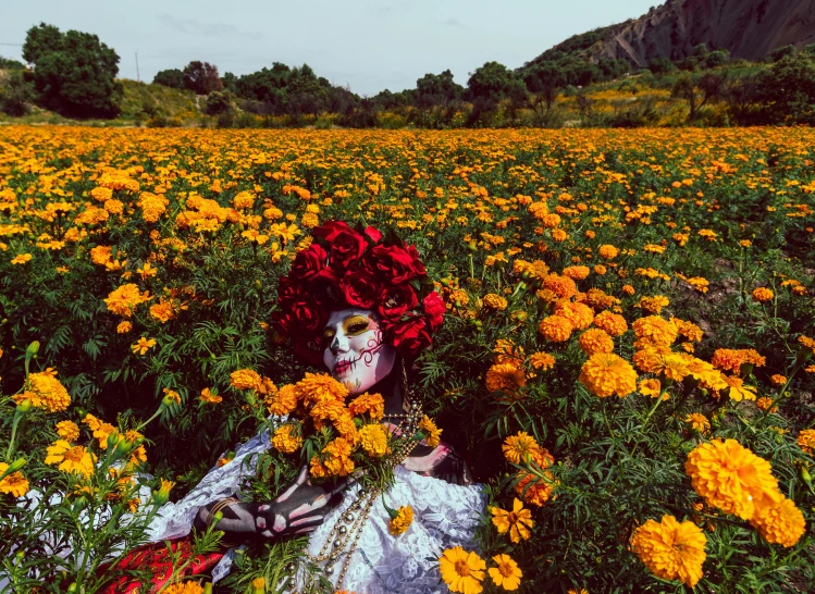 a woman with a skull face painted on her head laying in a field of yellow flowers