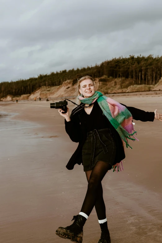 woman in black coat on beach holding camera