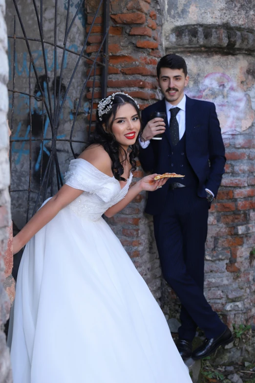 a beautiful young woman holding a pizza next to a man in a suit