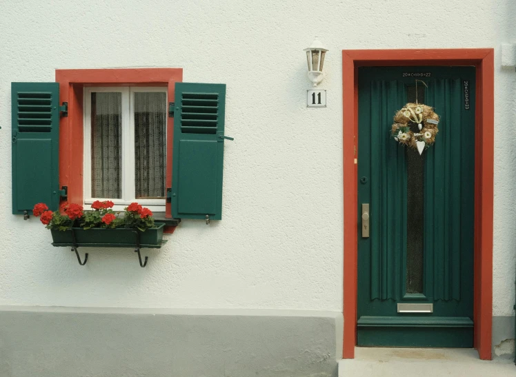 a house with red flowers and a green shuttered door