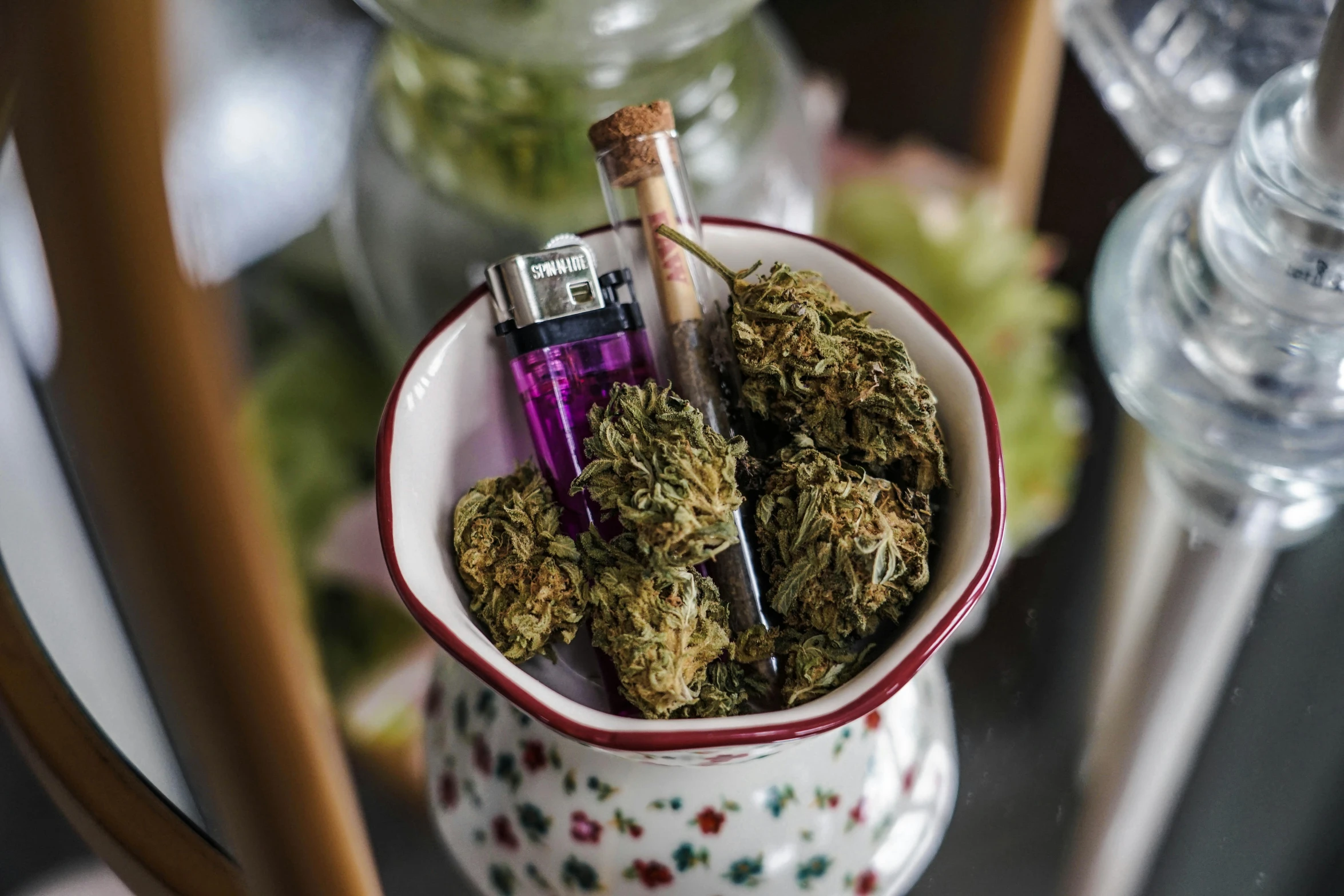 a small cup with marijuana and lighter sitting on a glass surface