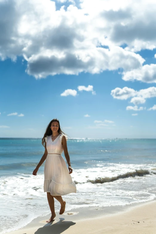 a beautiful woman in a dress walking down the beach