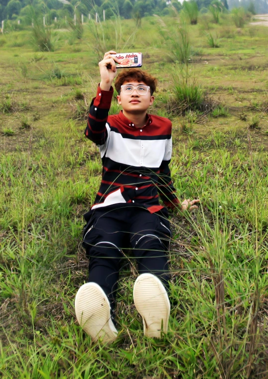 a  in striped shirt sitting on the ground holding up his hat