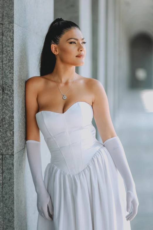 a woman in white dress leaning against wall