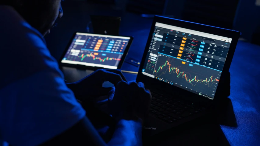 the person sits in front of two computers with different indicators on their screens