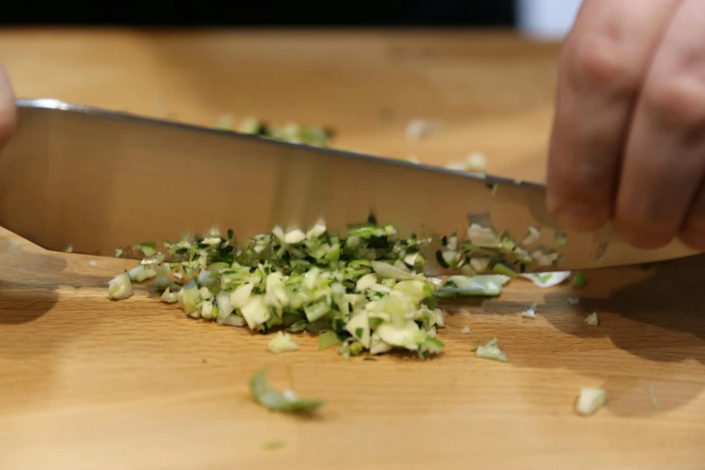 someone cuts up green and white onions with a large knife