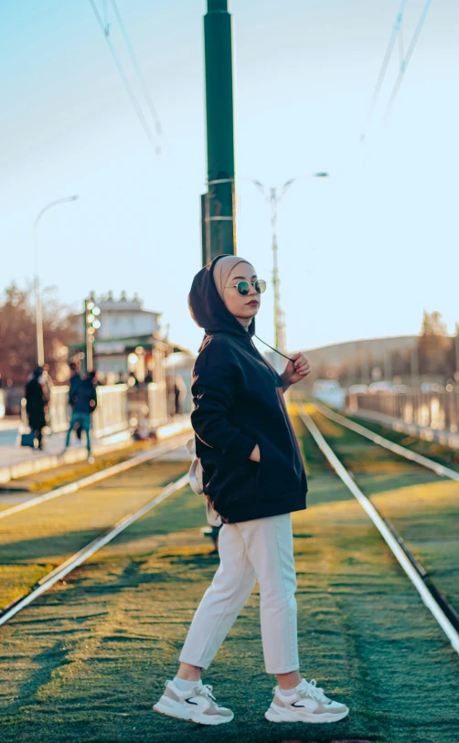 a woman in a hijab walking next to train tracks