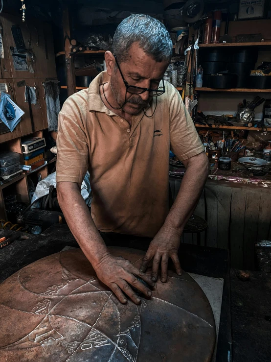 an older man in his tool shop carving a leather material