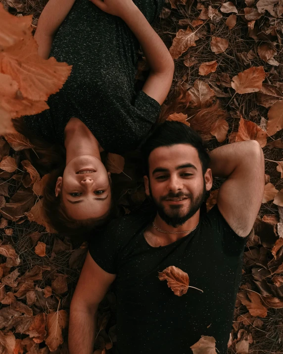 a couple lays on the ground in autumn leaves