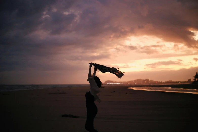 a woman is standing on a beach holding onto a scarf