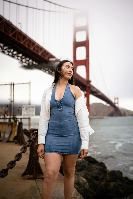 an asian woman in overalls by the water with the golden gate bridge in the background