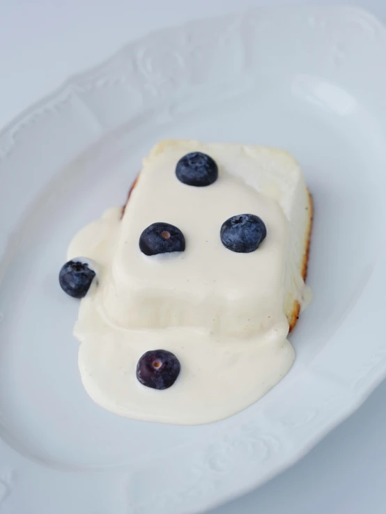 a white plate topped with a piece of cake and covered in blueberries