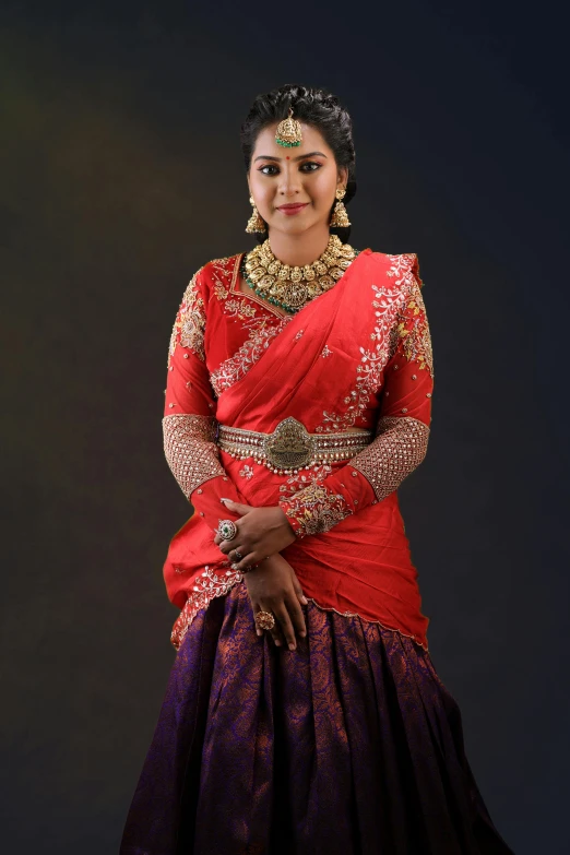 a woman wearing a bright red sari, standing in front of a dark background