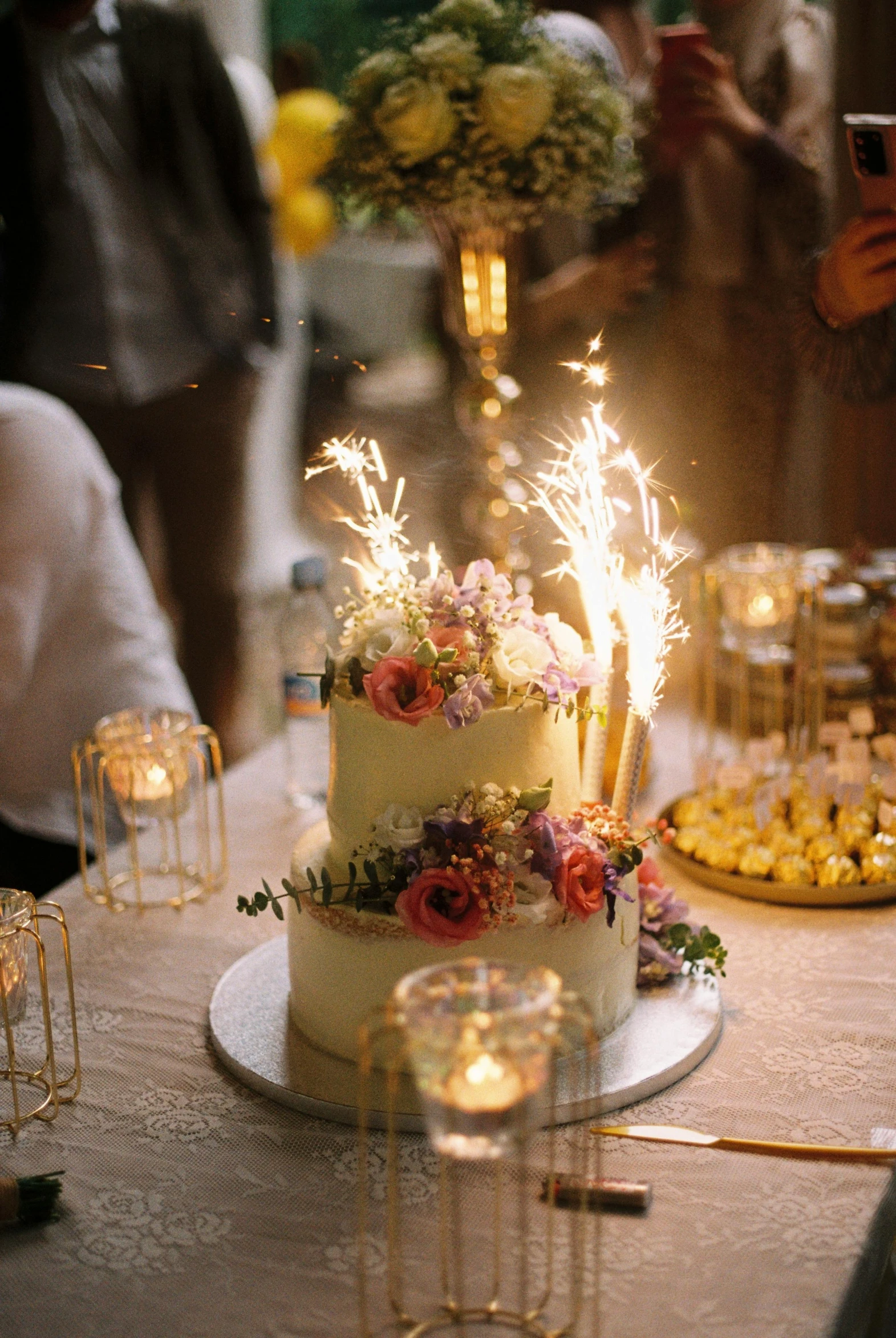 a three tier cake with bright lit candles and flowers