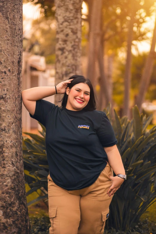 a woman posing with her hand in her hair, wearing a black shirt and tan pants