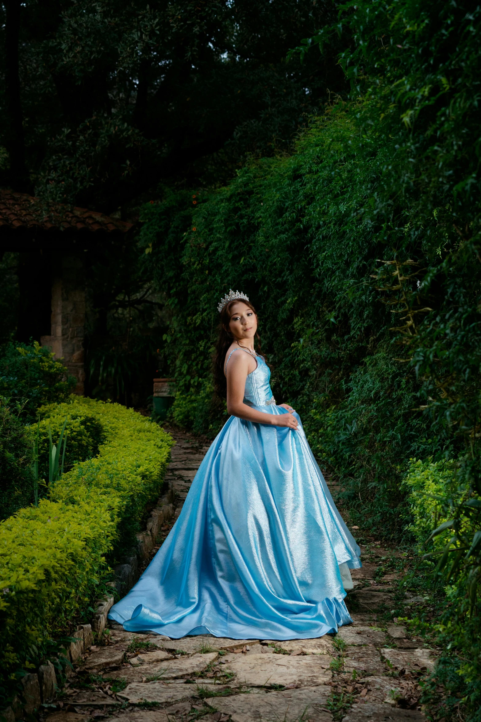 a beautiful woman wearing a blue ball gown stands on the steps of an ornate garden