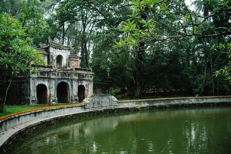 a small old house next to water with lush green vegetation around