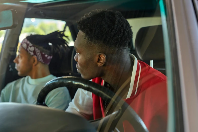 a man driving in a car with another man behind him