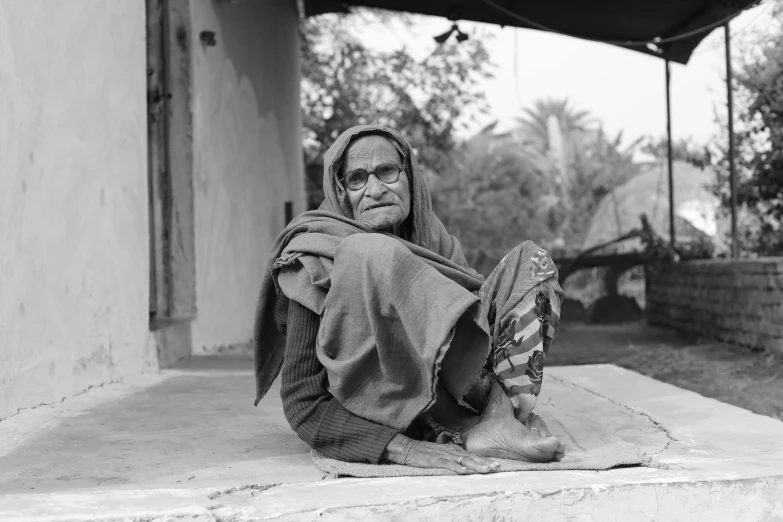 an old woman sitting on the floor with her blanket up to her face