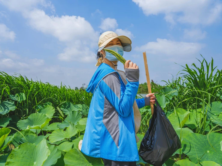 a woman wearing a hat and holding a plastic bag in a field