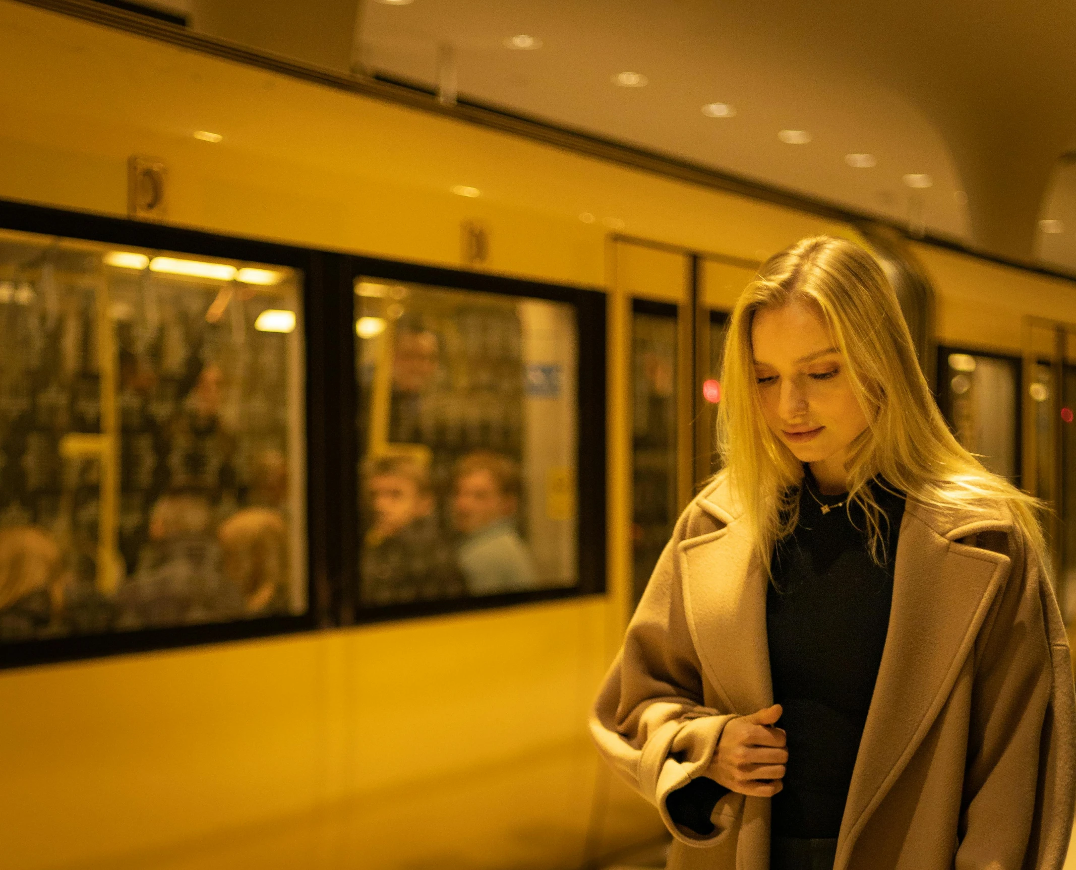 a young woman wearing a coat stands near the subway train