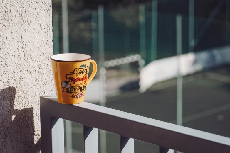 a coffee cup sitting on top of a balcony near a tennis court