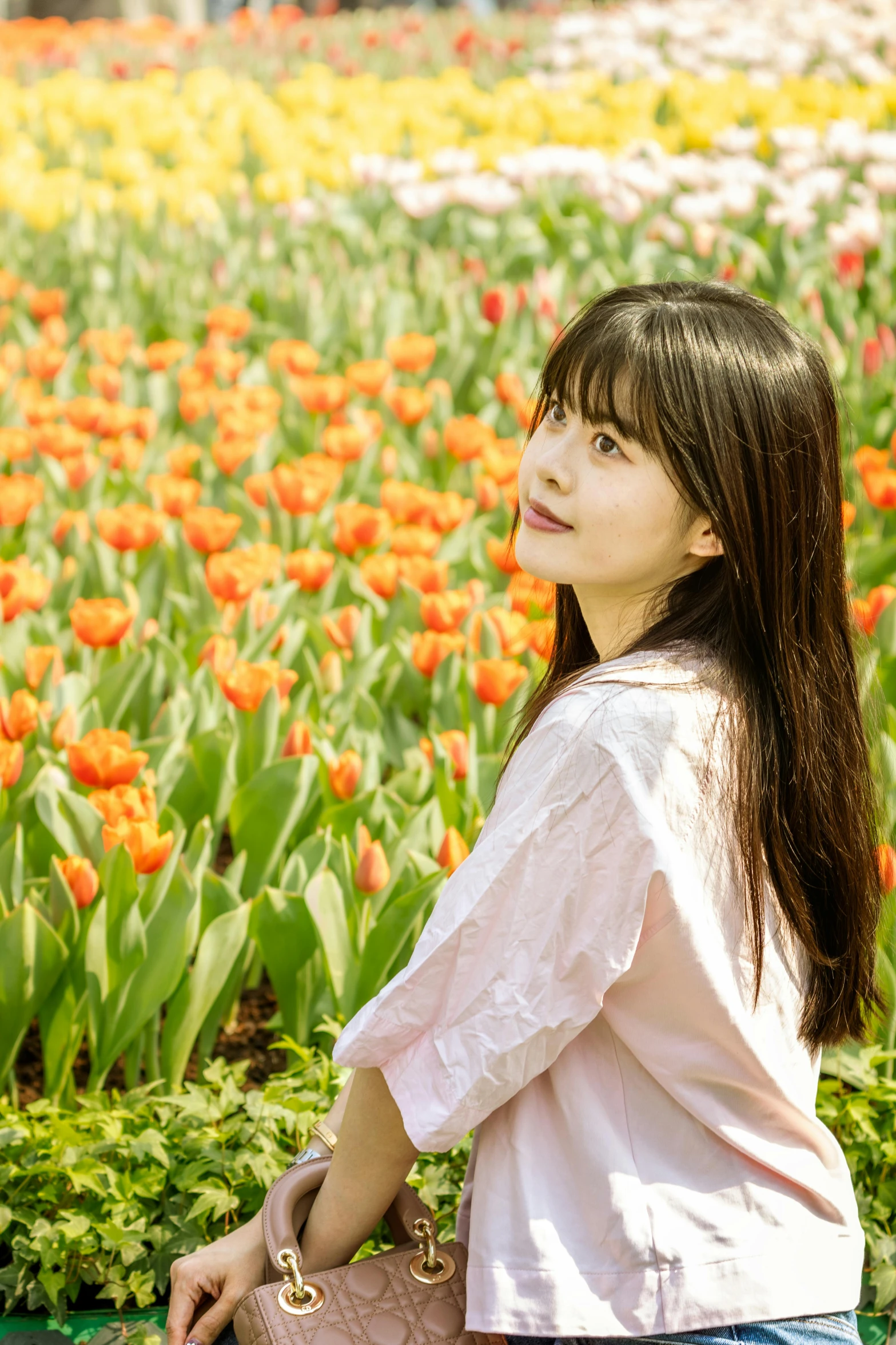 a woman standing next to a field with lots of flowers