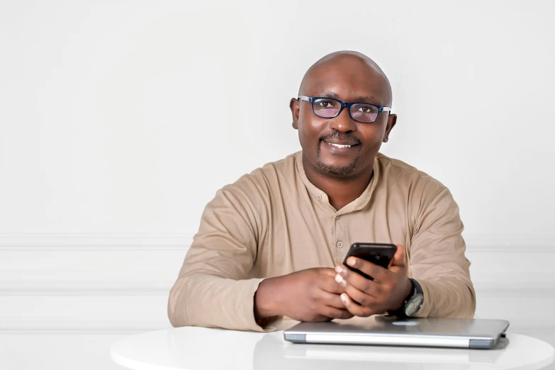 man smiling while holding his cell phone near the laptop computer