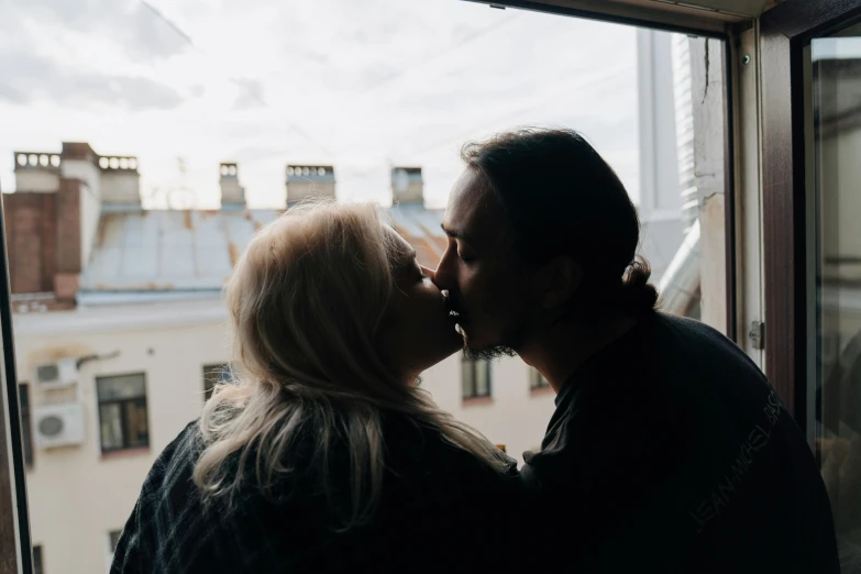 a couple sharing an intimate kiss in front of a window