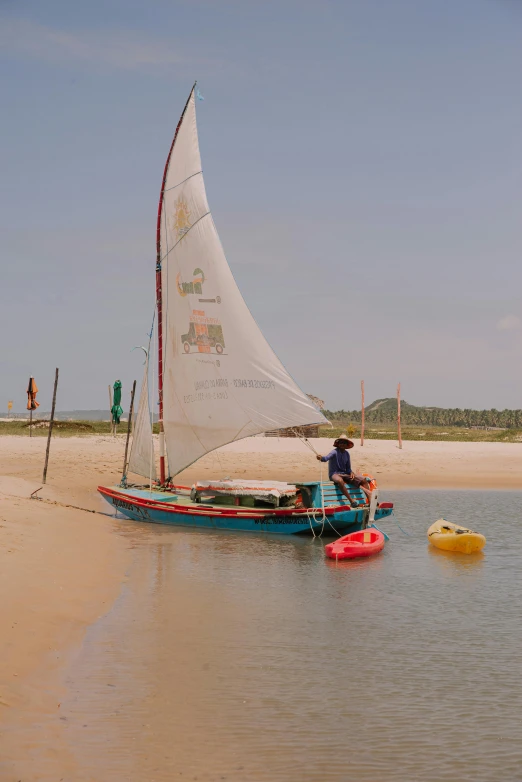 a sail boat sits on the beach with two small yellow rafts