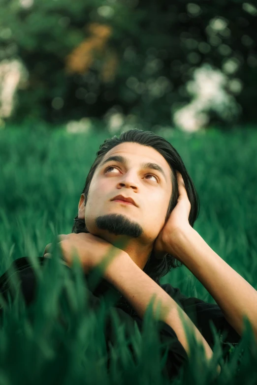 a man laying in the grass with his hand on his chin