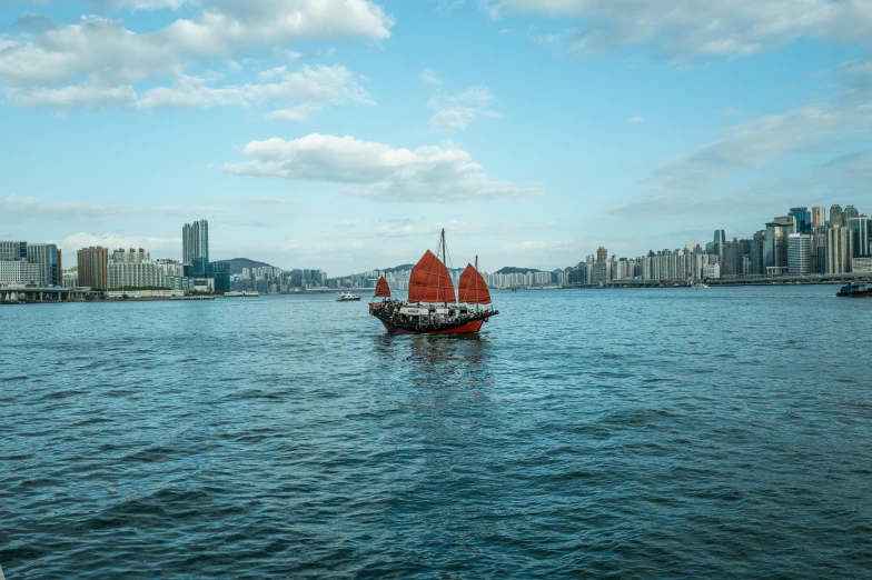 a tall sail boat floating in a bay by some tall buildings