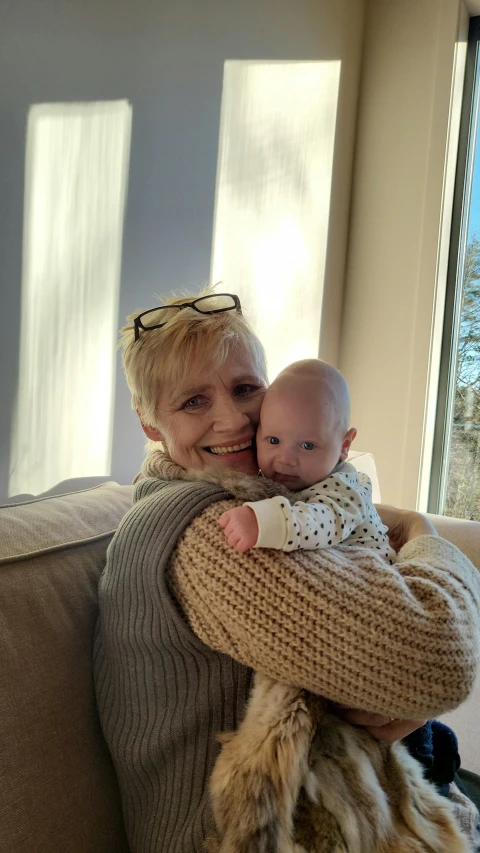 an older woman with white hair and a sweater holding her baby