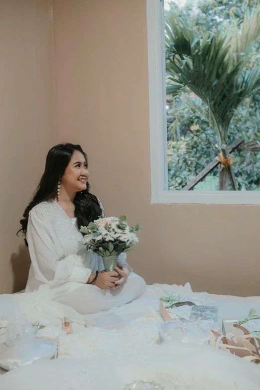 a woman is sitting on the bed and she has flowers in her hands