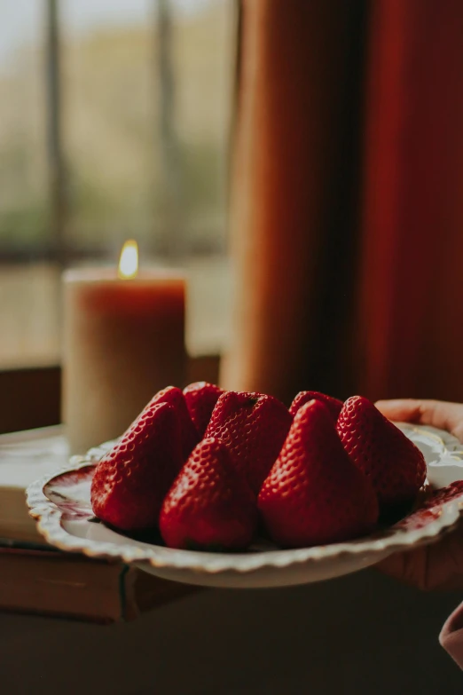 several sliced strawberries sitting on a plate near a candle