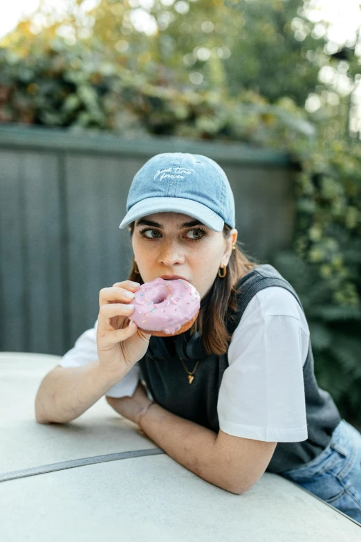 a woman in black shirt and cap sitting down eating a donut