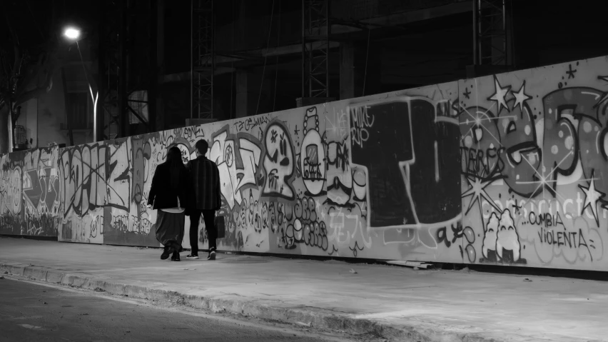 two people are standing against a wall with graffiti