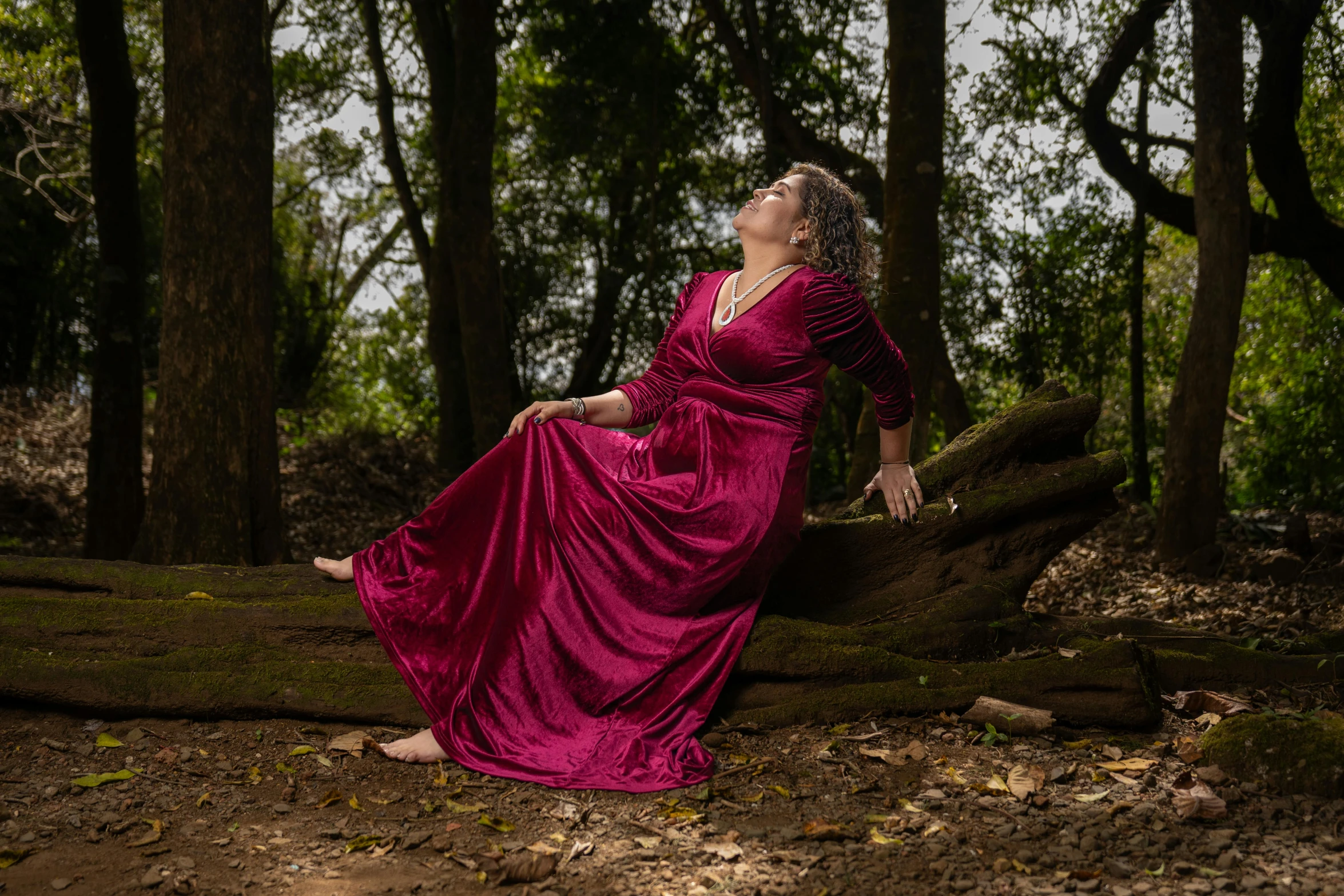 a woman sits in the woods wearing a red dress