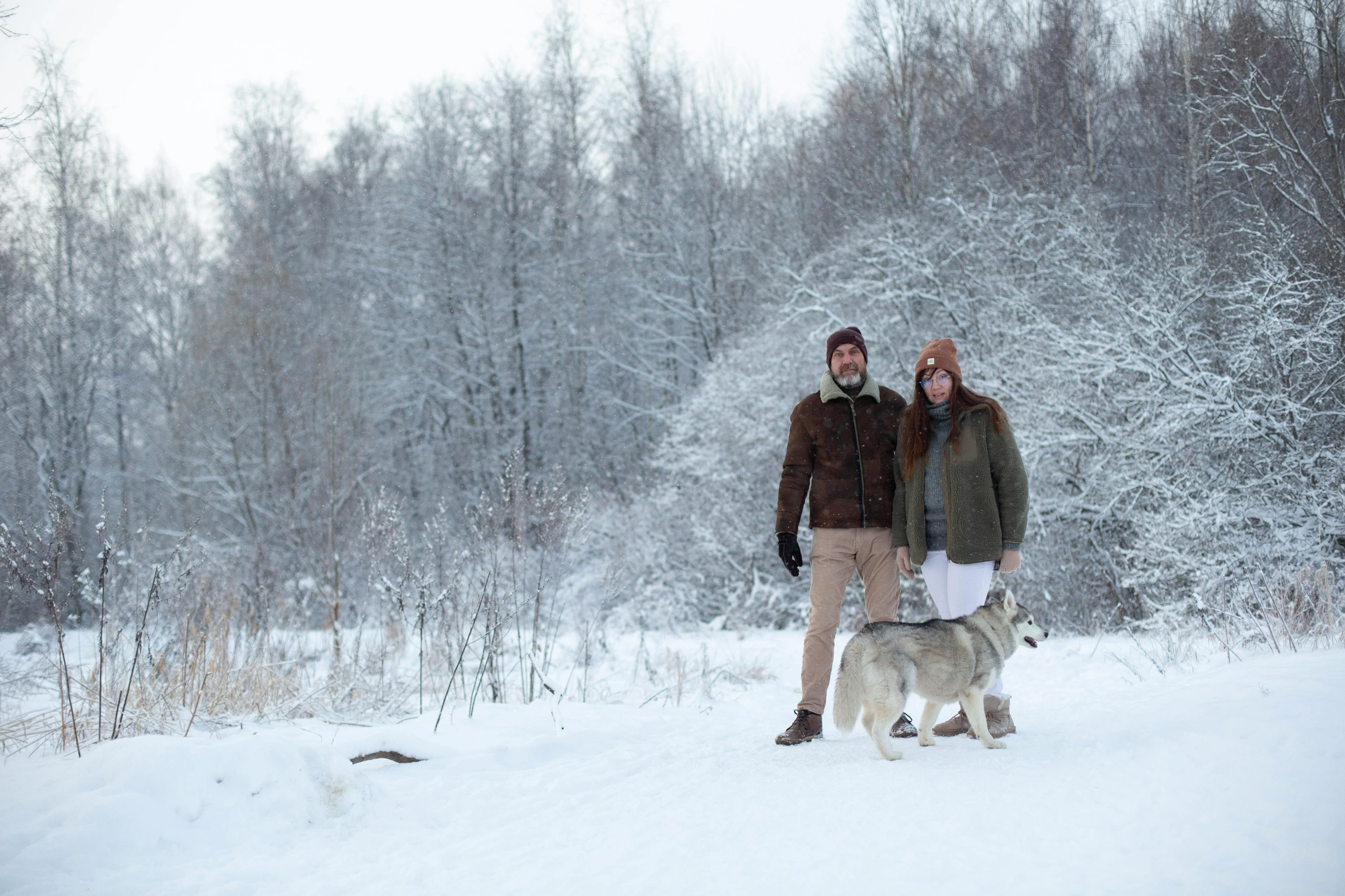 a couple on a snowy hill posing for the camera with their dog