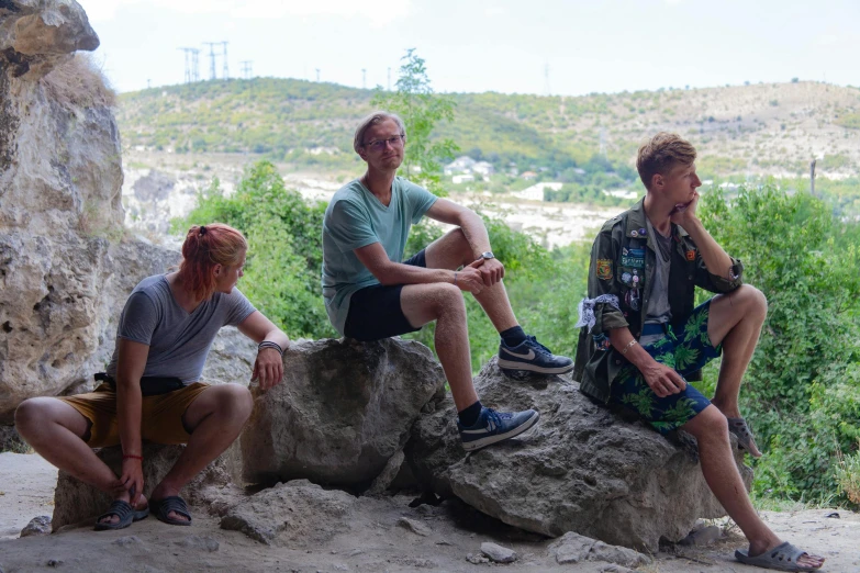 three men on a rock with mountains in the background