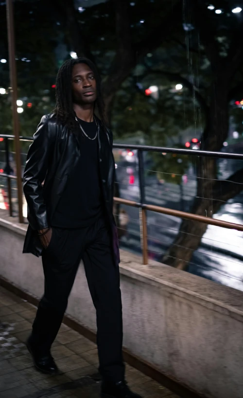 a young man in black walking by the water