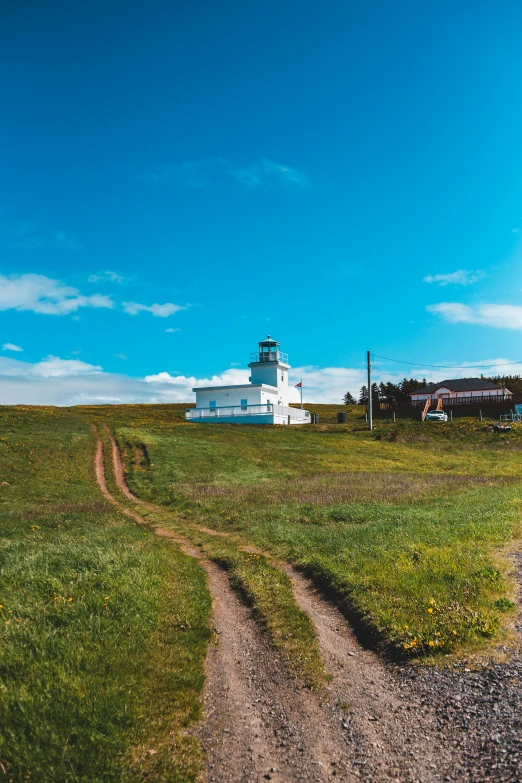 a dirt road runs through a green grassy field next to a building