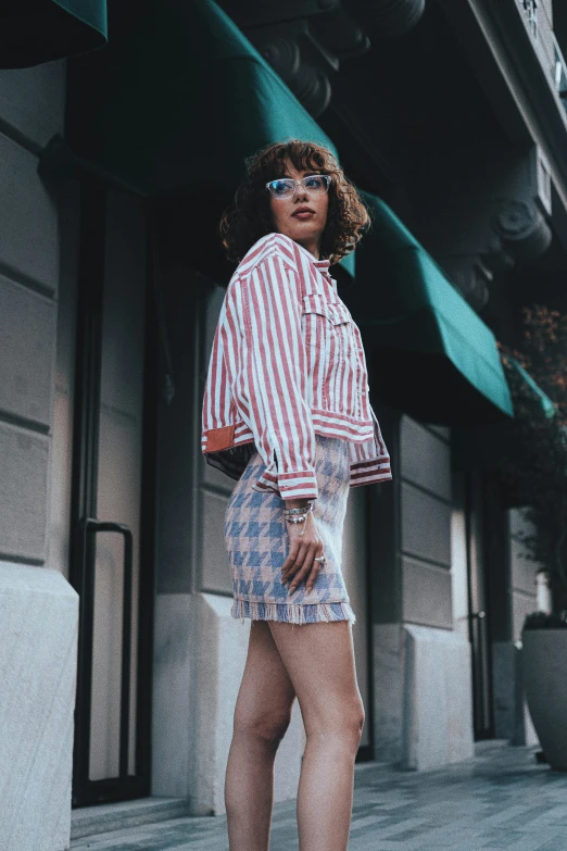 a woman in plaid shirt and shorts standing by a building