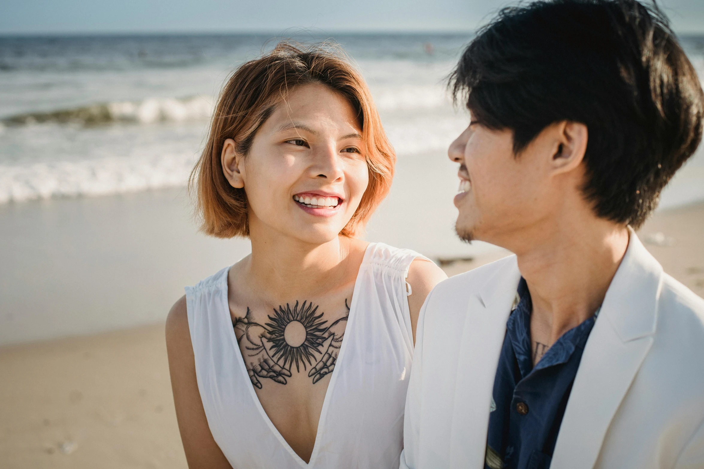 a woman standing next to a man in front of a ocean