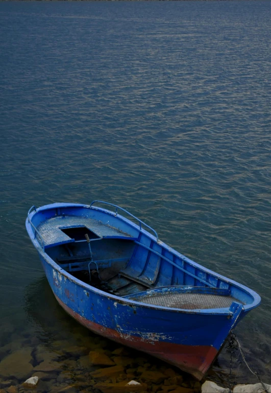 a small blue boat sitting next to rocks in the water