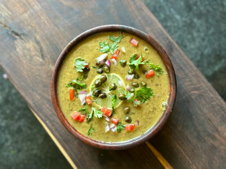 a brown bowl filled with soup and toppings on top of a wooden  board