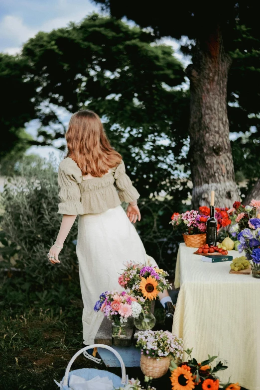 a woman in a dress and basket standing near a table with flowers