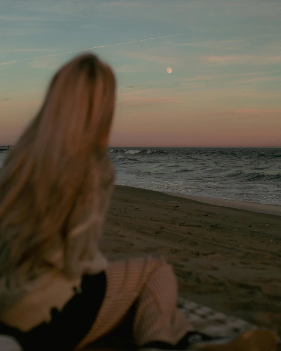 a beautiful blond sitting on top of a bed in front of the ocean