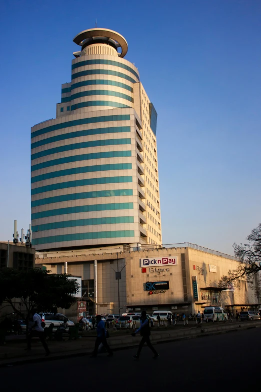 a building with a large round top and dome shaped window, stands tall, in front of people on the sidewalk